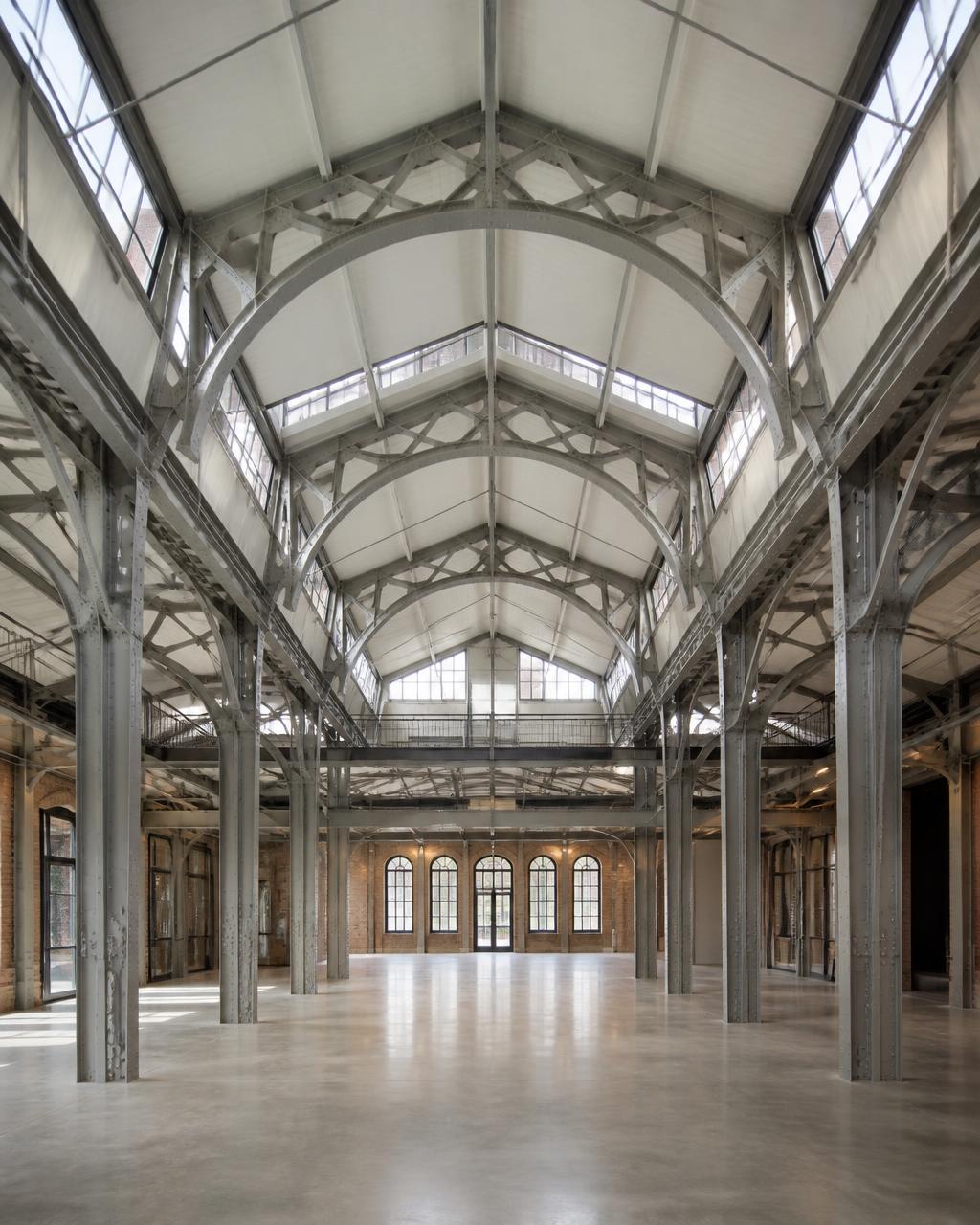 Halle métallique de 1902 réhabilitée, charpente rivetée apparente et sol libre